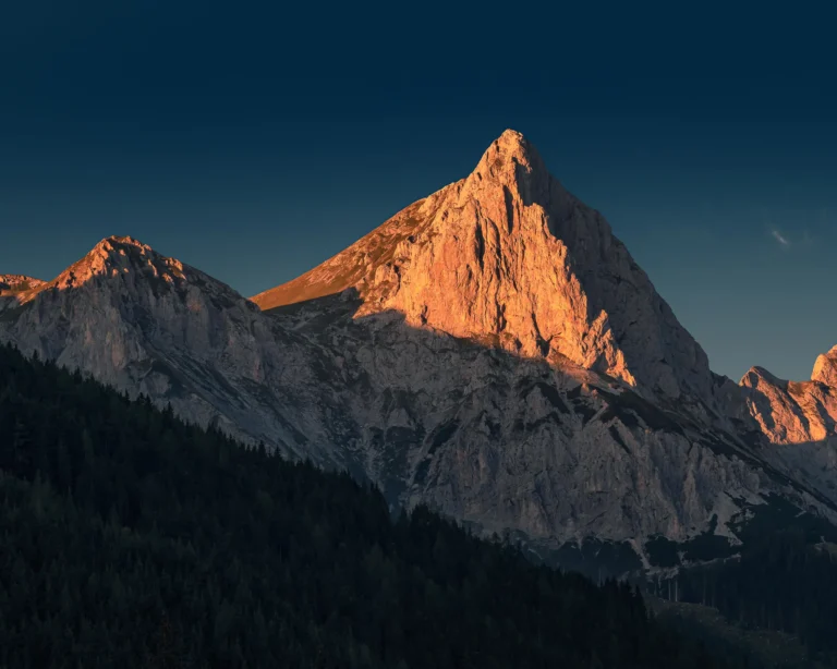 Sunlit alpine peak glowing in golden hour light against a deep blue sky.