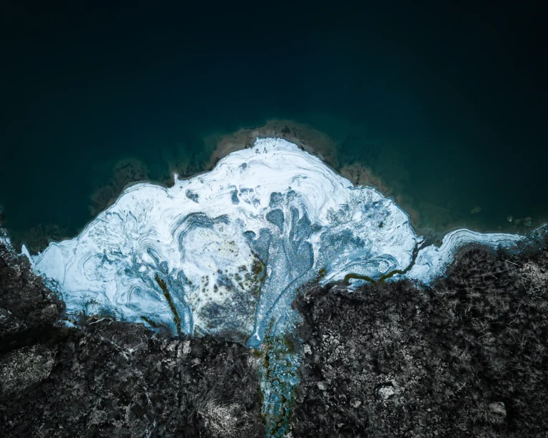 Aerial drone photograph of swirling ice patterns along a Norwegian glacier edge meeting dark water