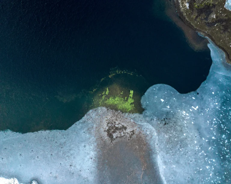 Aerial view of ice patterns meeting dark water along a Nordic shoreline.
