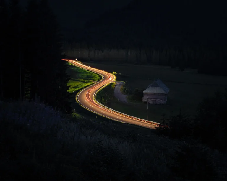 Long exposure light trails curving along a dark road through forested landscape at night in Austria