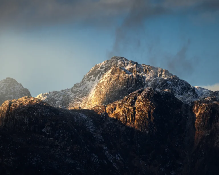 Takket fjelltopp som fanger gyllent sollys over skyggelagte dalsider i Norge