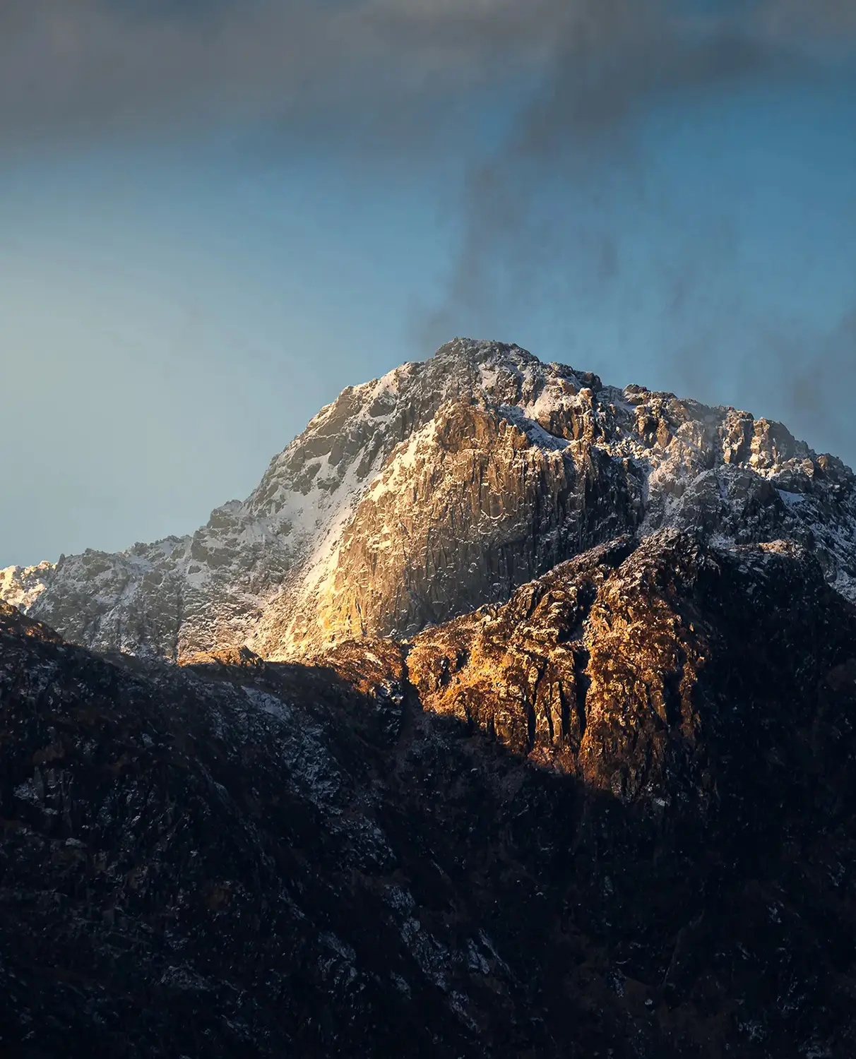 Sunlit snow-capped mountain peak against a dramatic sky.