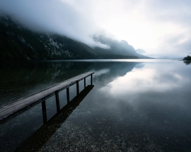 Wooden pier stretching into the still, foggy waters of Lake Bohinj surrounded by misty mountains