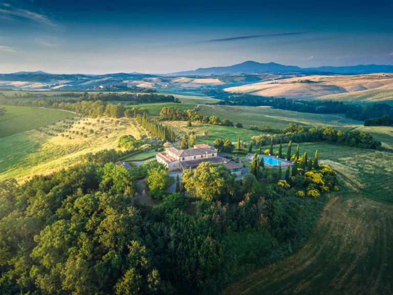 Dronefoto av en toskansk villa omgitt av bølgende grønt landskap i Italia