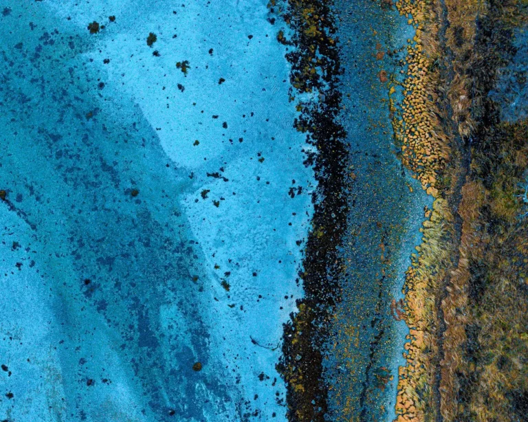 Flyfoto av turkise kystfarvann som møter en mørk, ru strandlinje i Norge