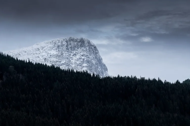 Massiv snøkledd fjelltopp under tunge, grå skyer i Norge
